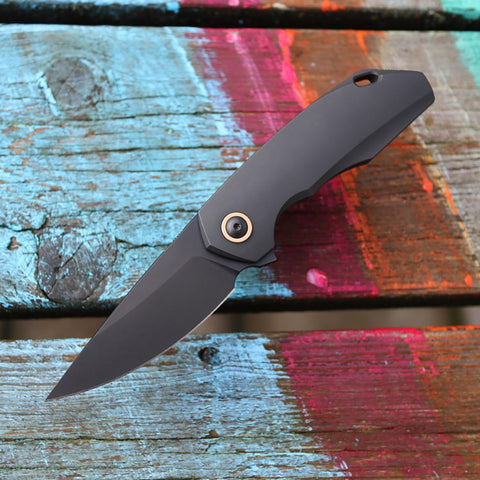 GiantMouse Knives GMP6 Integral Titanium Folder with PVD finish and M390 Blade Steel and bronze pivot ring, presentation side fully open on painted wood